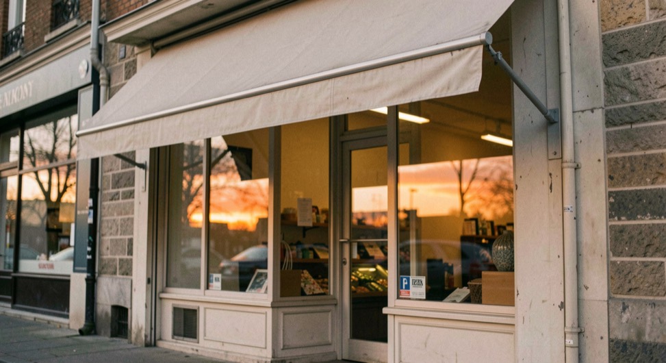 Une devanture de commerce en fin de journée, store à demi baissé et reflets orangés sur la vitre